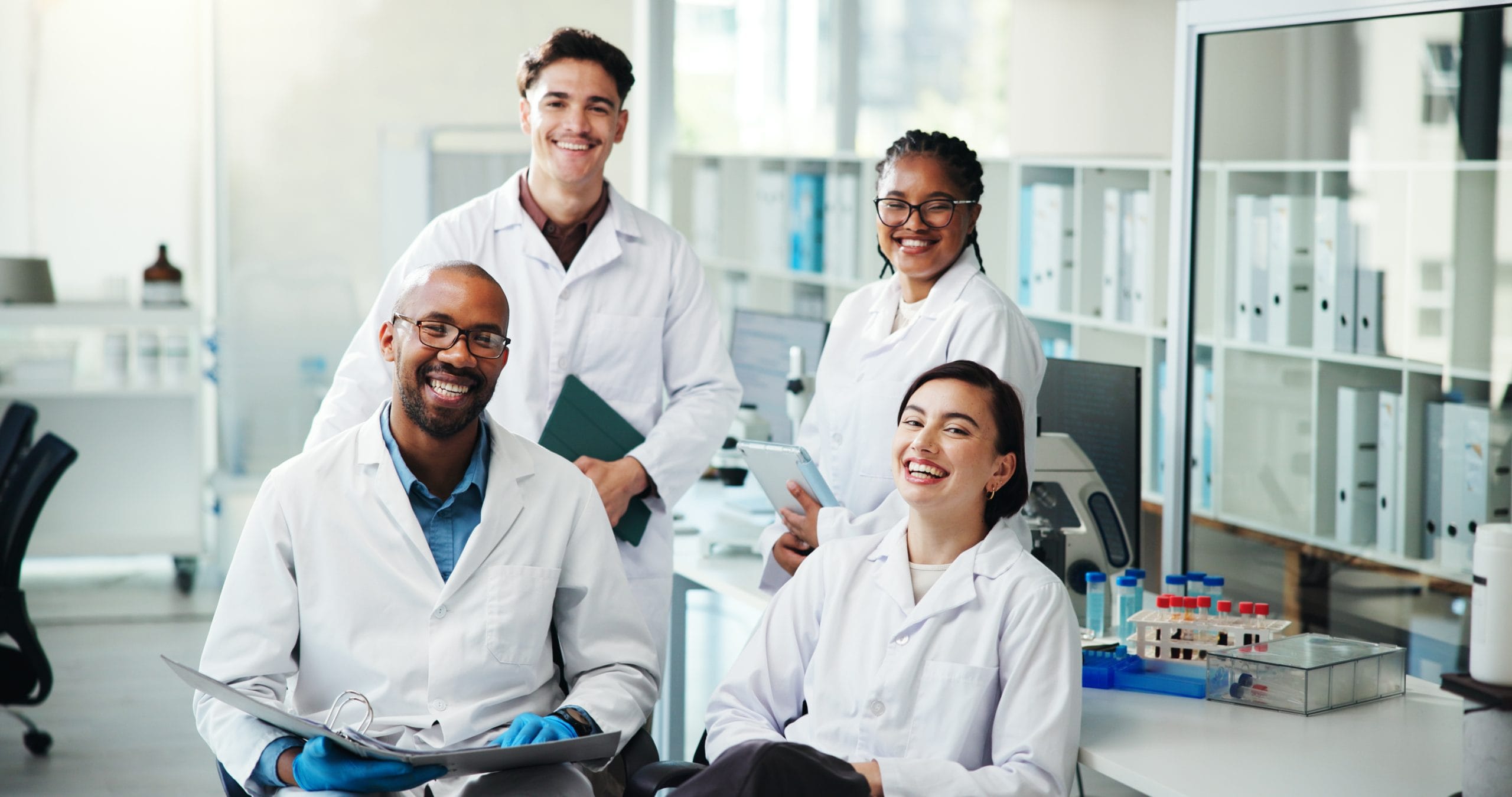 A team of smiling medical professionals in a modern laboratory, representing the skilled healthcare workforce supporting Jamaica for cancer care.