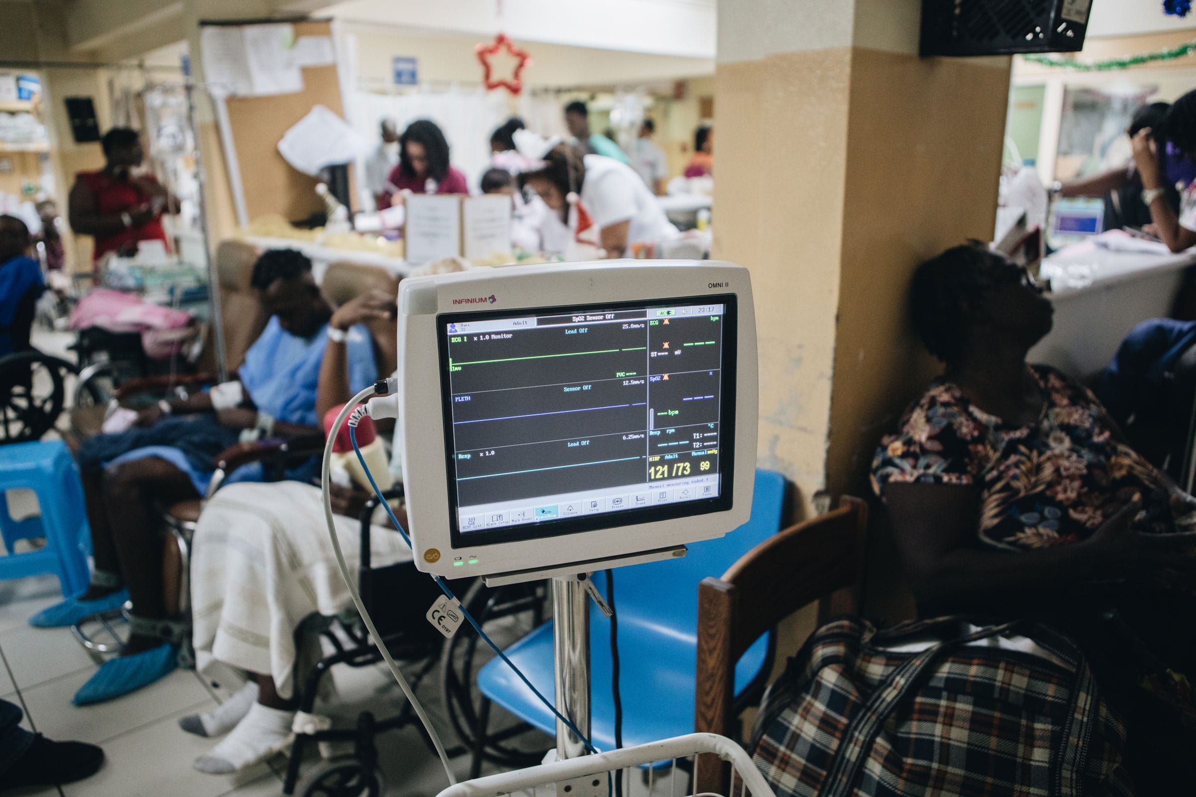 A busy hospital ward in Jamaica with patients receiving care and a vital signs monitor in the foreground, reflecting the realities of healthcare in Jamaica.