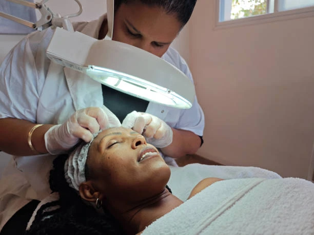 Dermatology services in Runaway Bay Jamaica, showing a professional skincare specialist performing a facial dermatology treatment under a magnifying lamp.